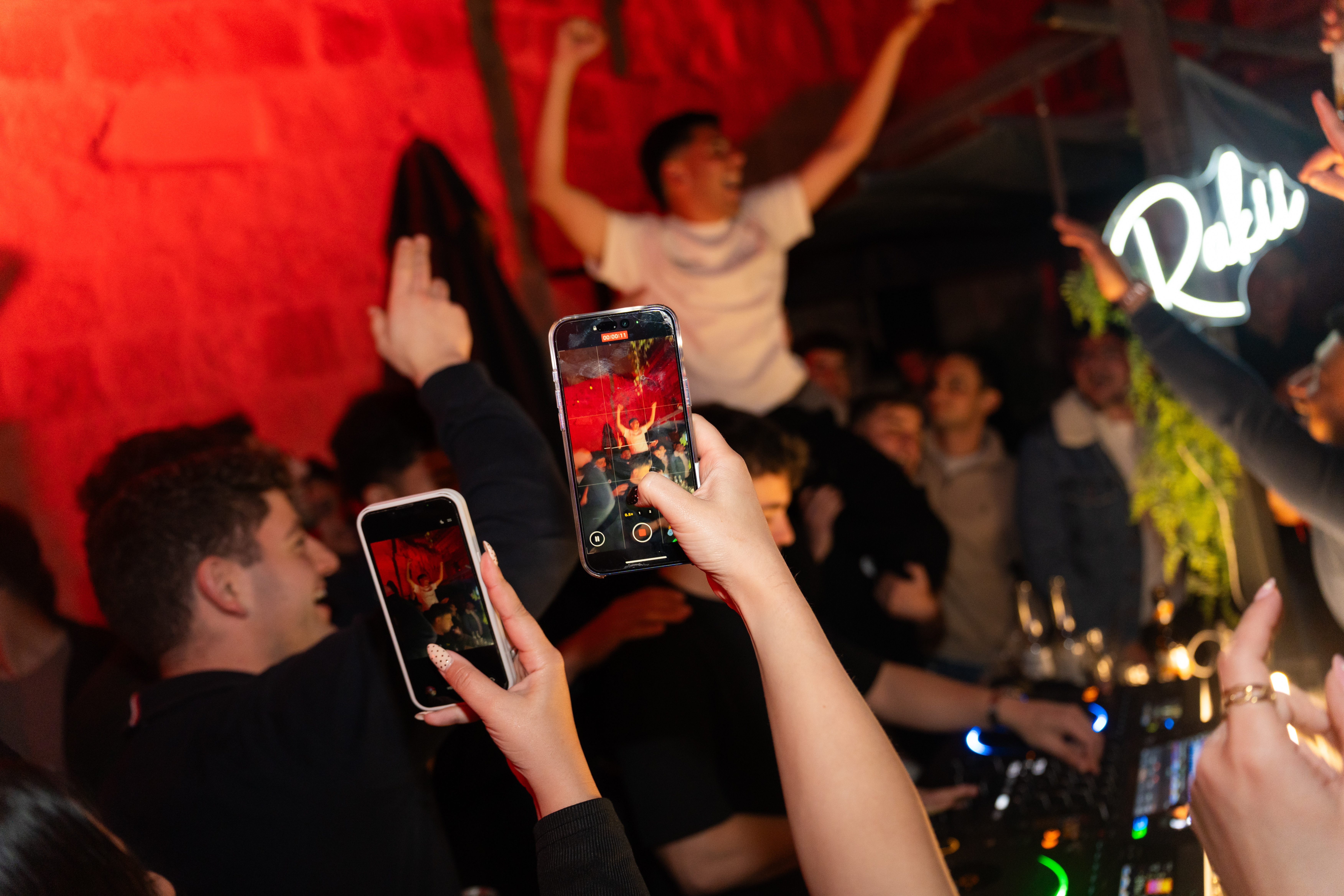 Crowd filming with phones, Rakii neon sign in background