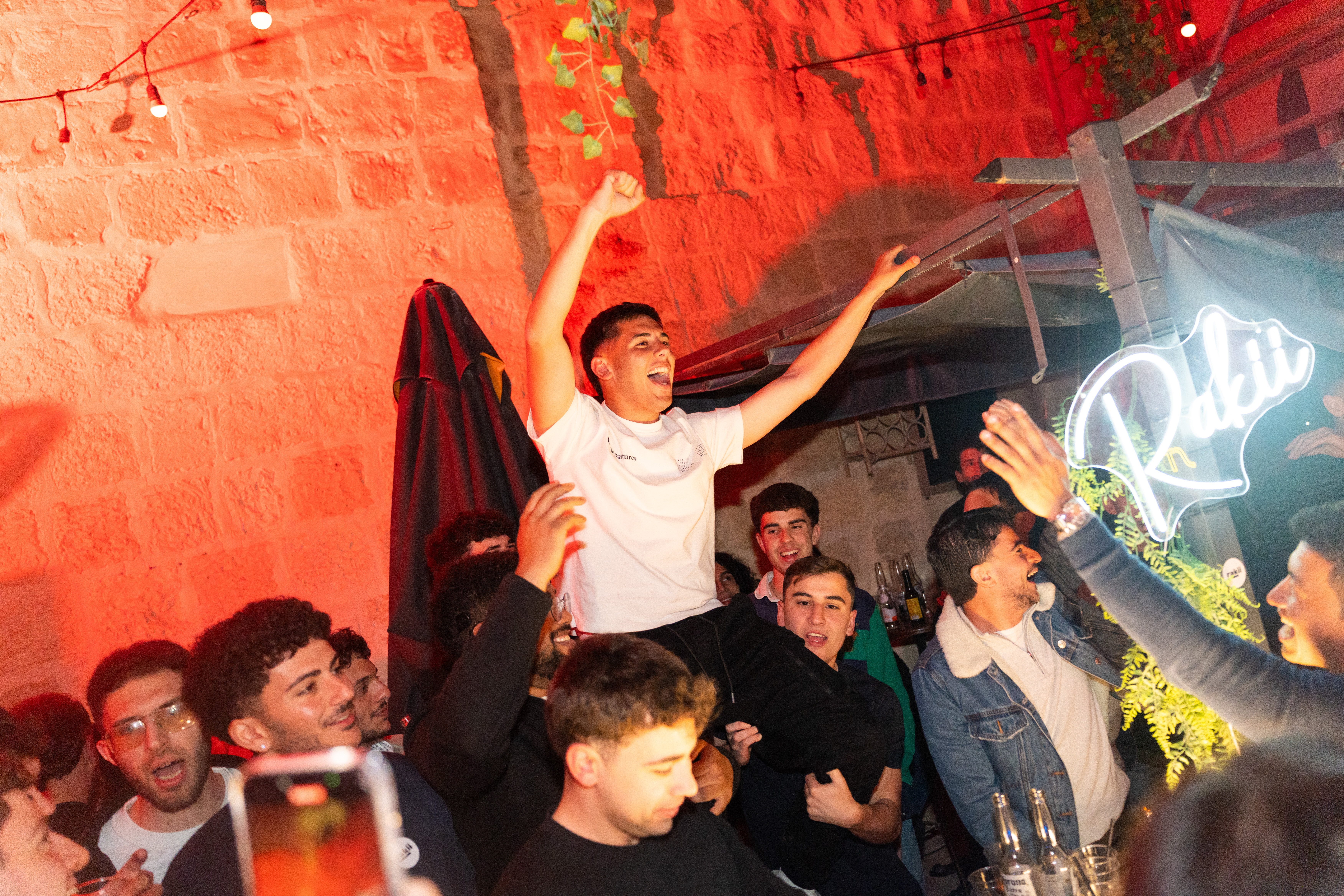 Person lifted on shoulders celebrating at Rakii, neon sign visible