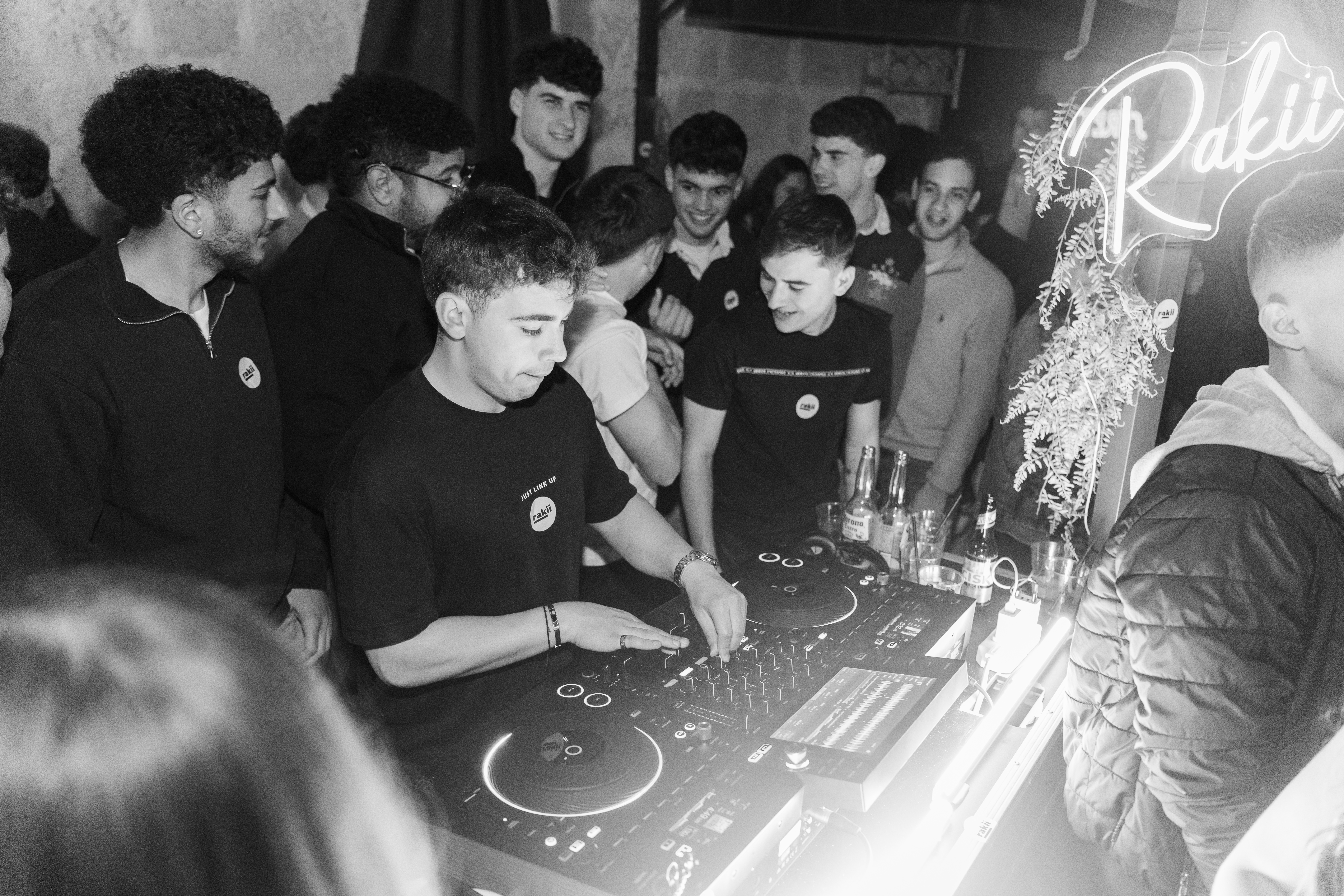 DJ at the decks with Rakii neon sign, black and white
